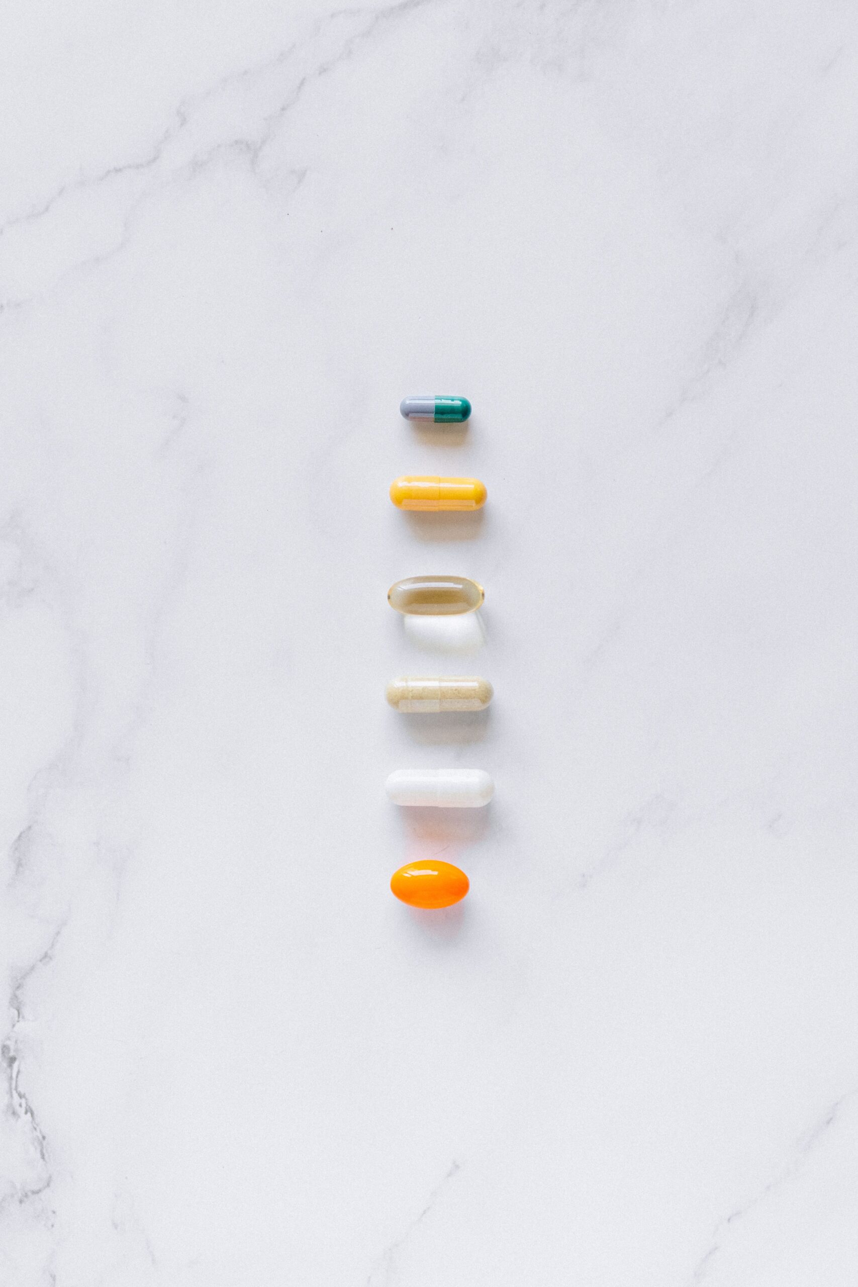 A vertical arrangement of assorted capsules and pills on a white marble background.
